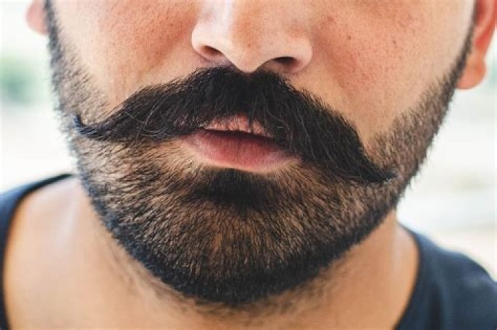 a man with a beard wearing a gray suit and grey shirt is looking at the